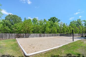 an empty volleyball court in a park with a fence and trees at Reserve of Jackson Apartment Homes, Jackson, Mississippi